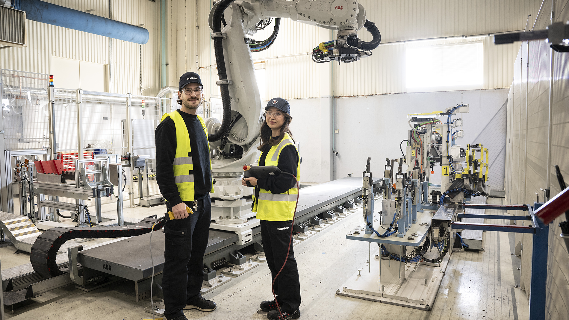 Två personer står framför en robot i en robotcell vid en handdator