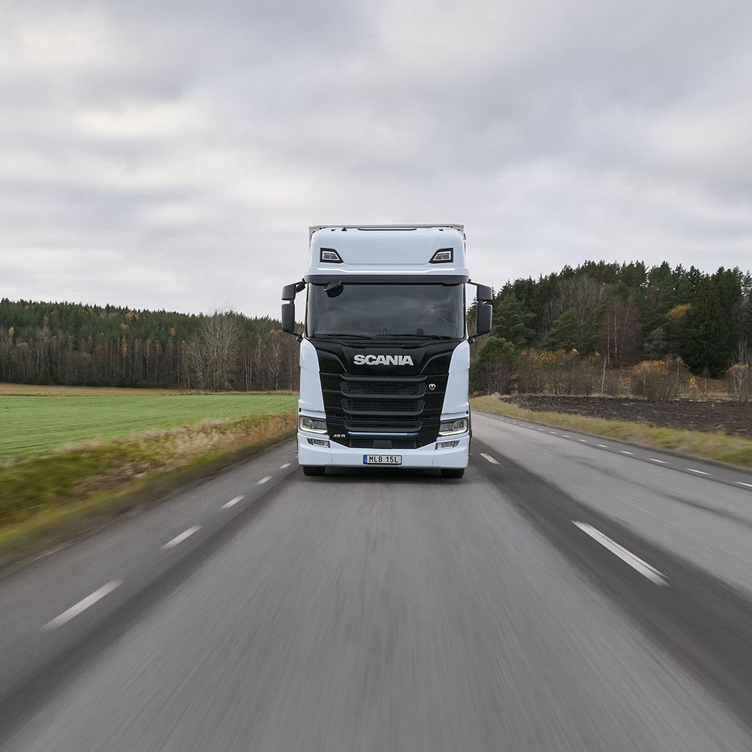 Scania ellastbil på landsväg vid grönt fält