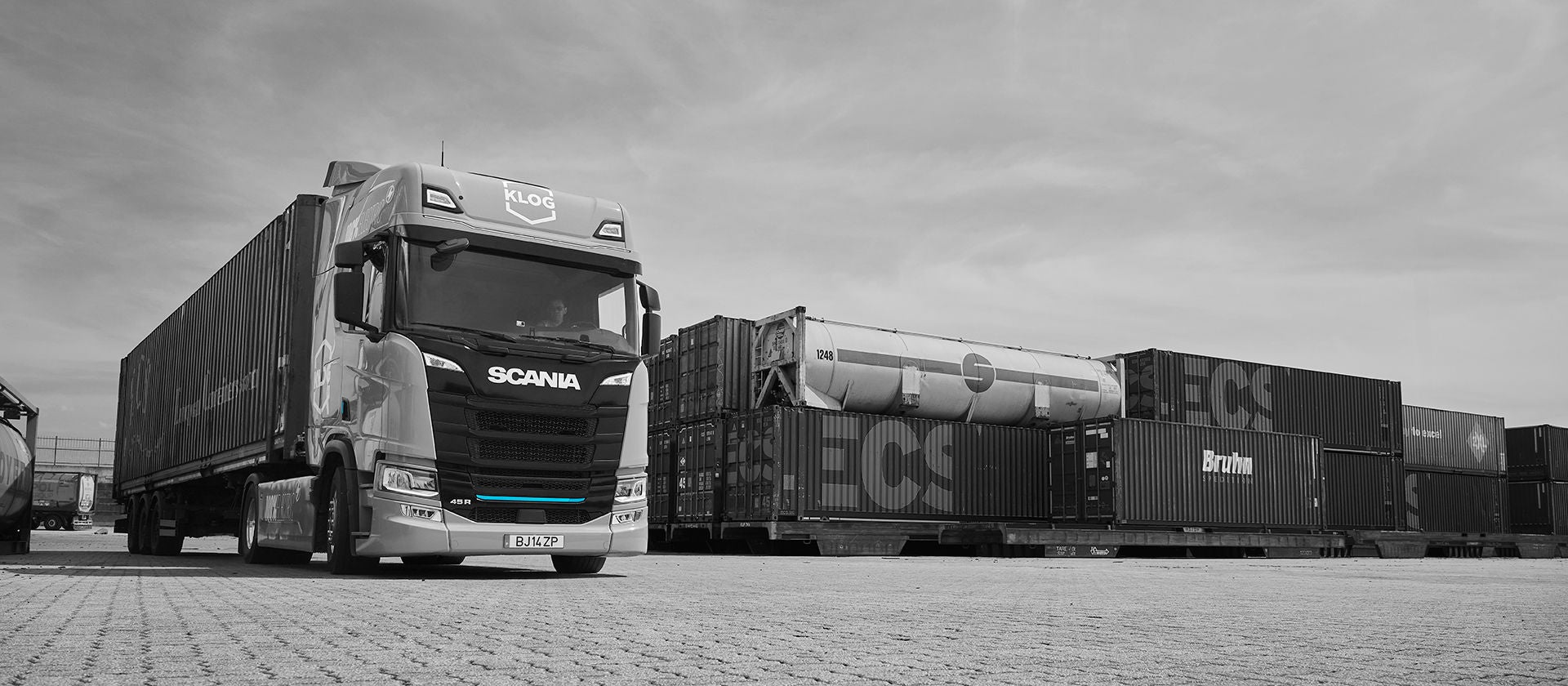 A black and white image of an electric Scania truck with shipping containers in the background, at the Port of Leixões in northern Portugal.