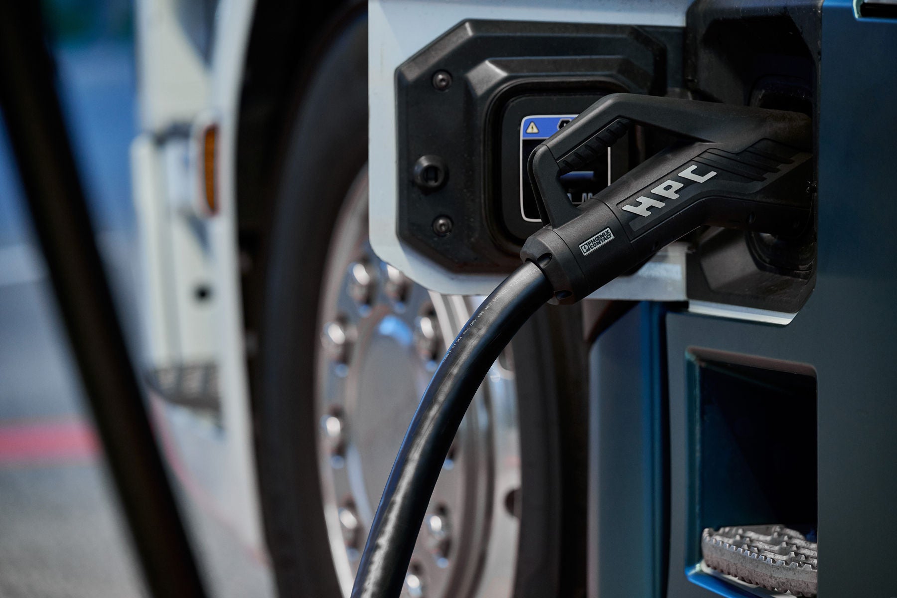 A high-power charging connector plugged into the charging port of a Scania battery-electric truck.