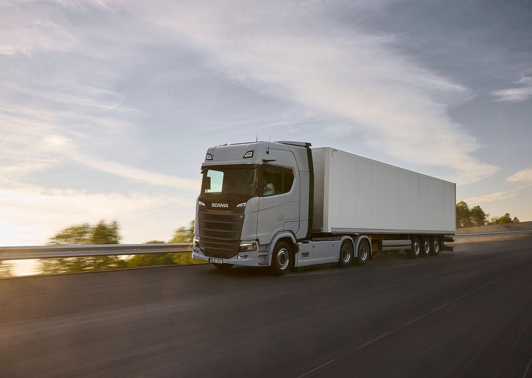A Scania Dynamic S-series tractor unit hauling a box trailer on a highway at dusk.