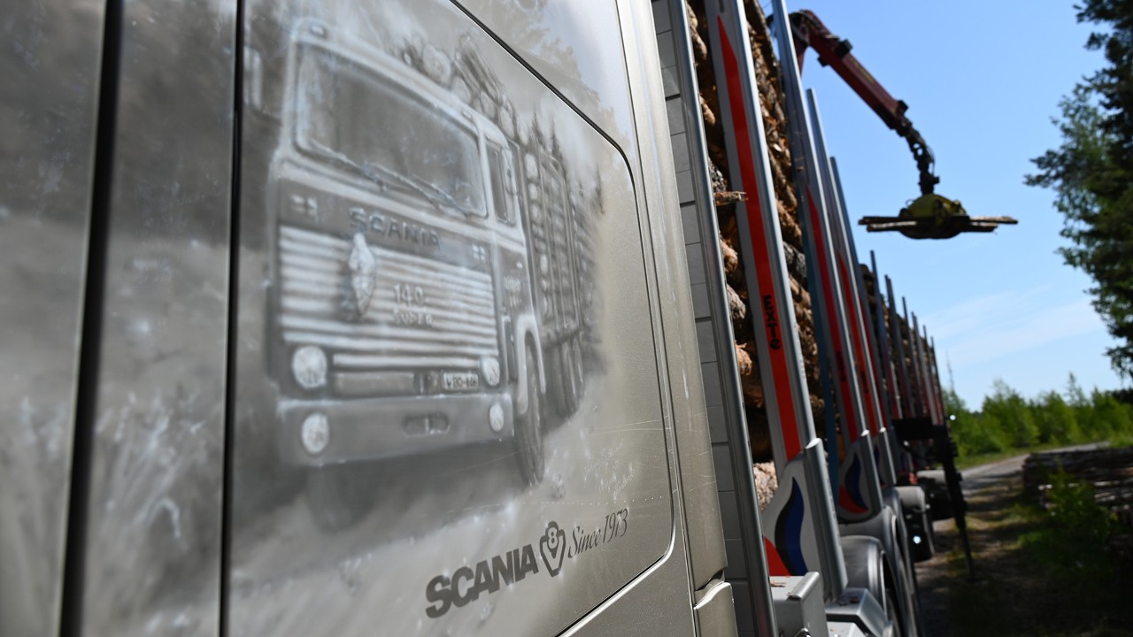Hopeanharmaista kyljistä piirtyvät esiin Johnny Sjöblomin upeat maalaukset, joissa Johan Antfolkin perheyrityksen ensimmäinen Scania 140 ajaa tukkia Michelin-ukko keulassaan. Kuva juhlistaa yrityksen 50-vuotista ajotaivalta. 