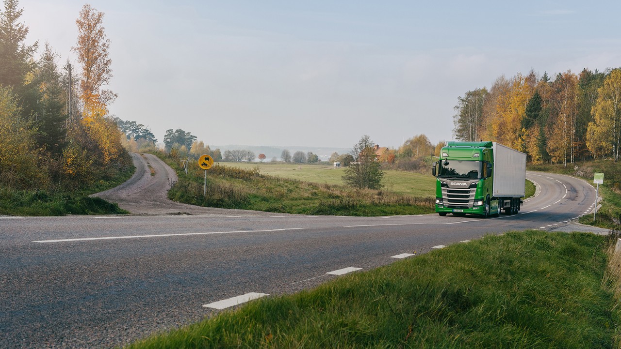 Grön Scanialastbil som kör ensam på en väg