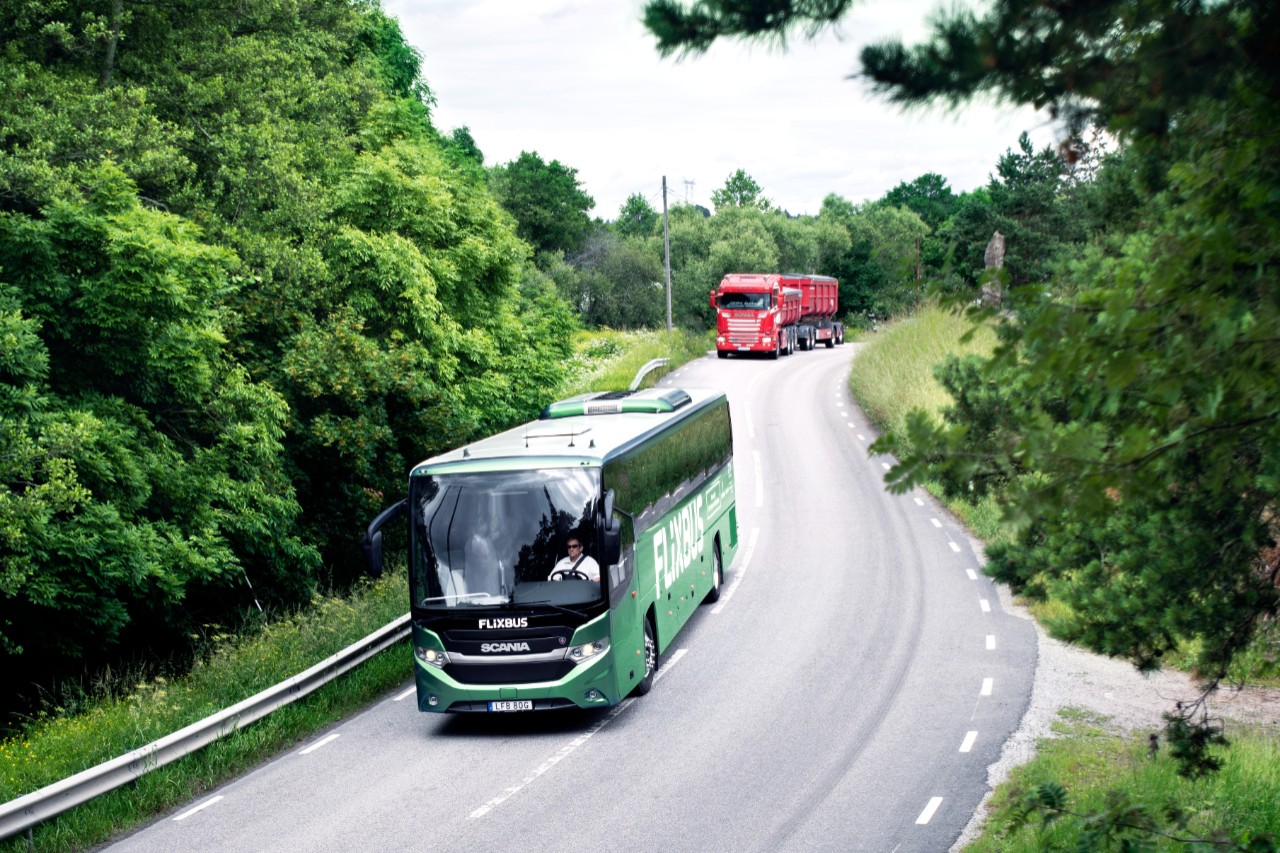 An alternative fueled Scania bus followed by an alternative fueled Scania truck on a road with greenery around