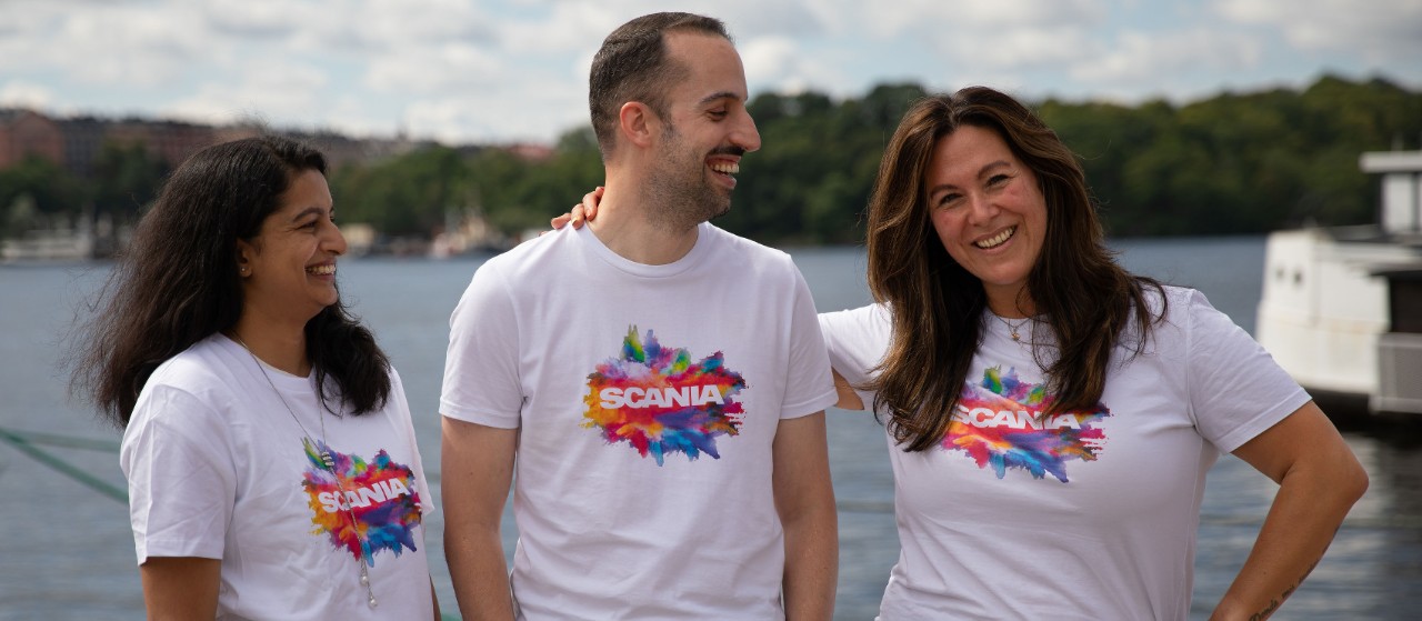 Three smiling Scania employees at Stockholm Pride in front of the water
