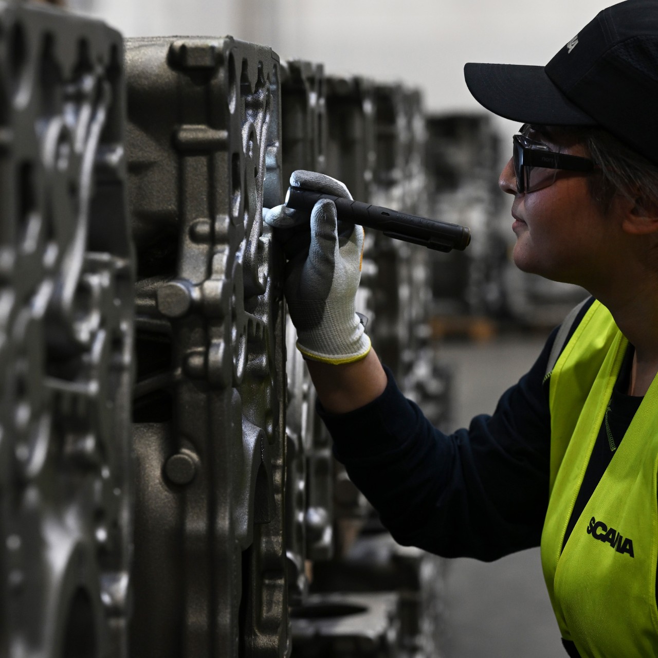 A female Scania employee shines a flashlight in Scania engine manufacturing.