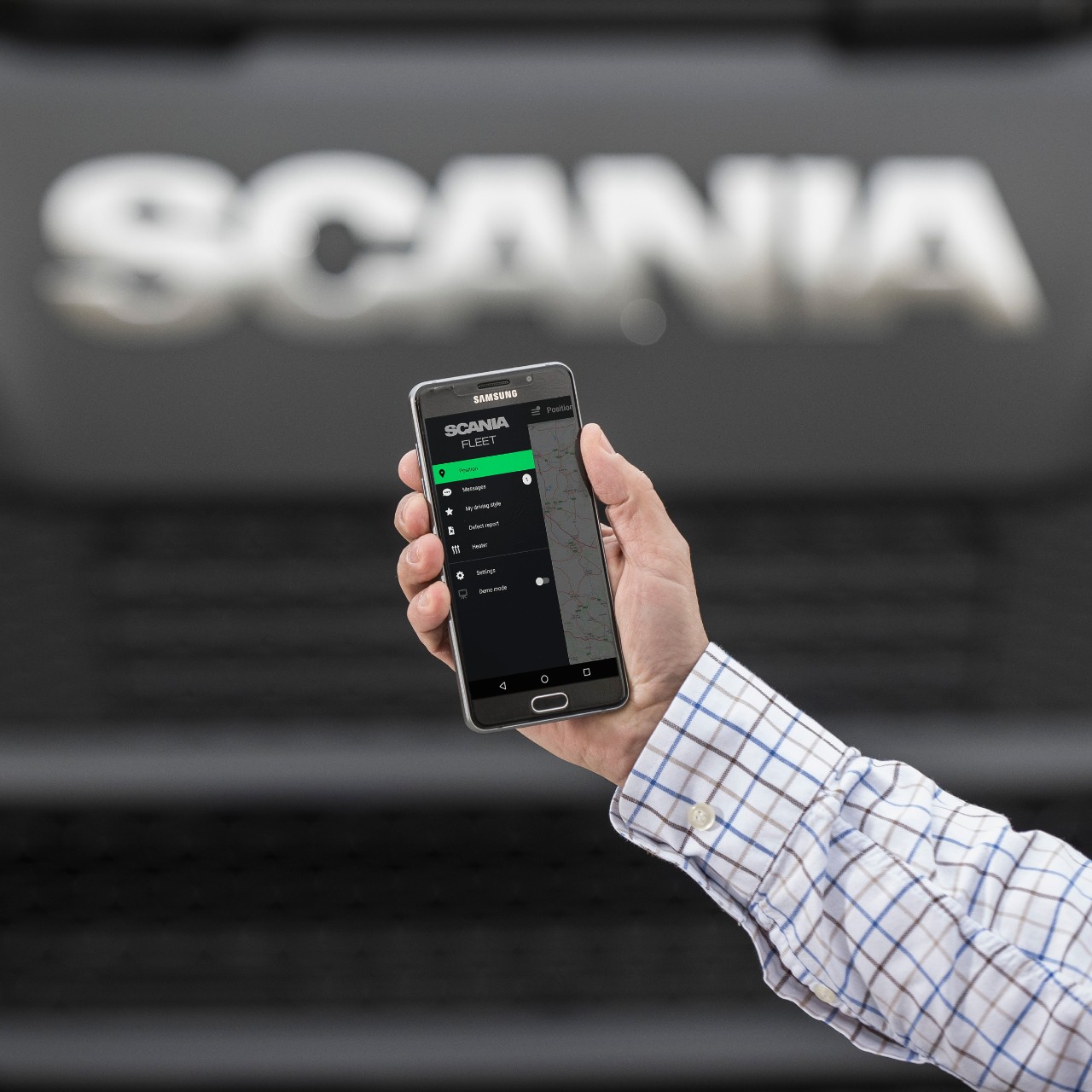 Håller i en smartphone framför en Scania