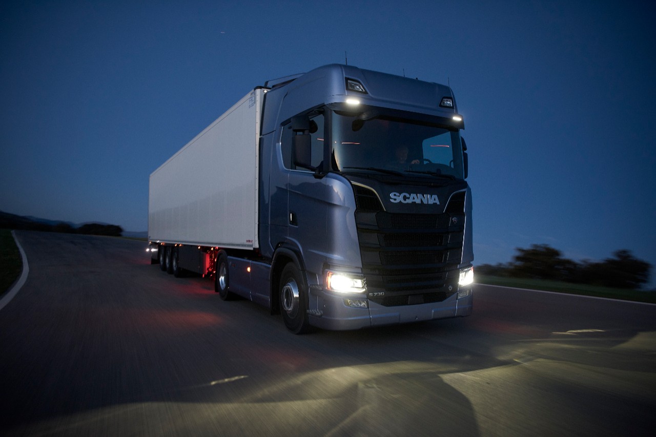 A Scania truck driving along a road at night