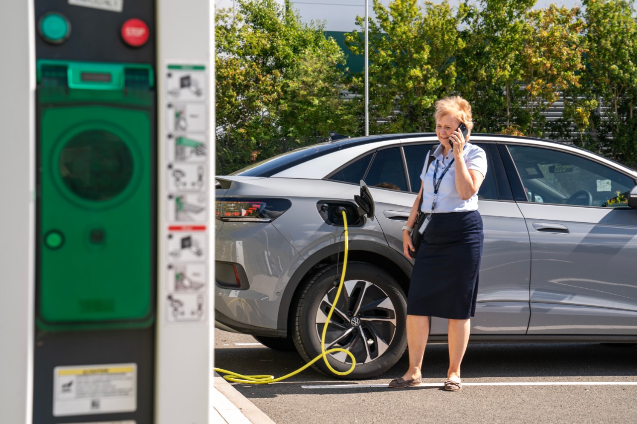 Woman on the phone standing next to electric car plugged in charging