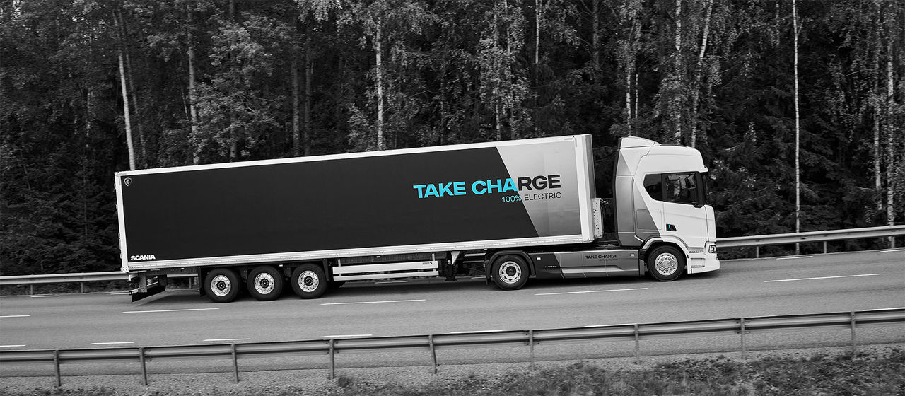 An electric Scania truck with a trailer with the words 'Take Charge' on it.