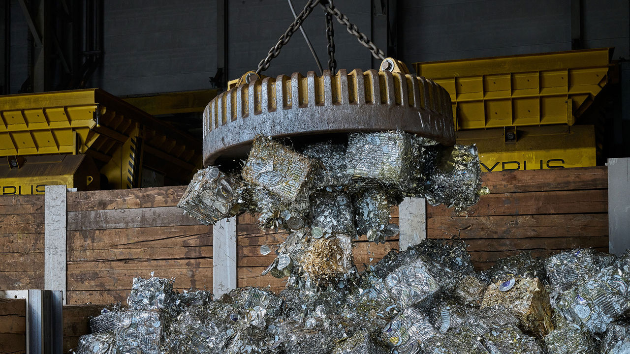 A powerful magnet lifts compressed scrap metal cubes ready for melting.